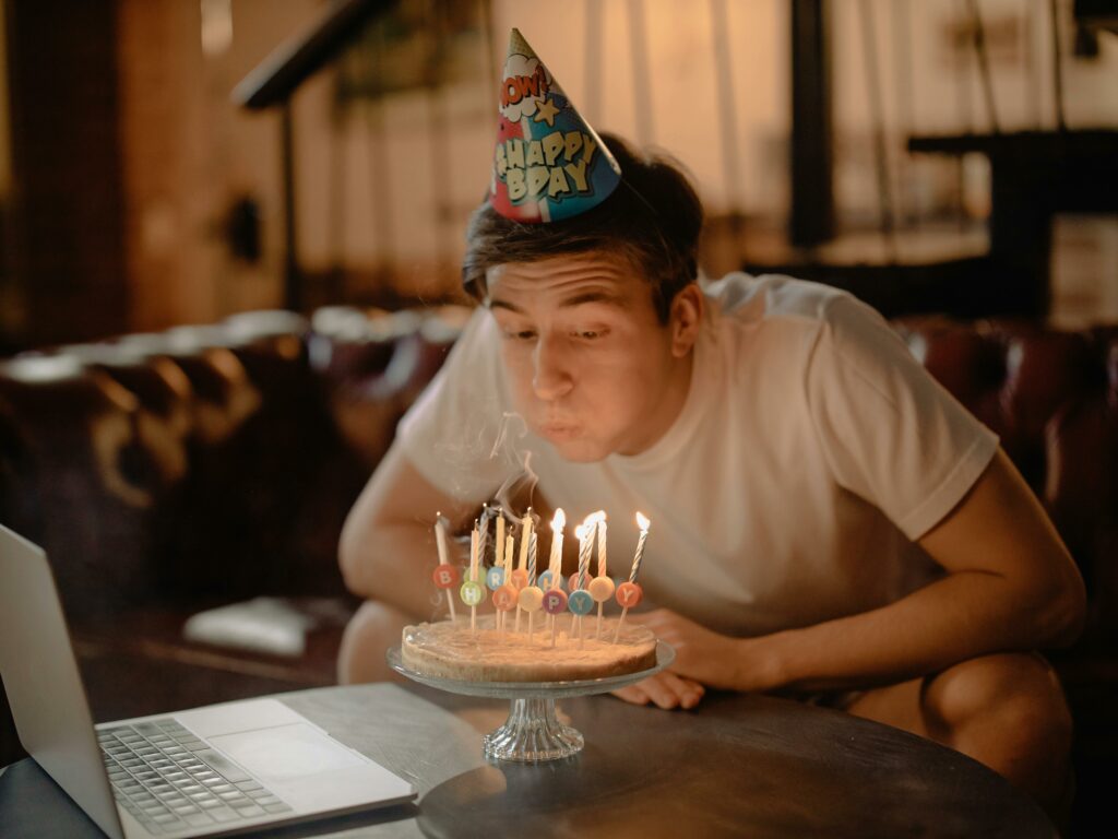 A man celebrates his birthday at home with a cake and online video call.